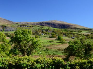 A countryside landscape with green fields trees and hills under a blue sky at 60 Hyfrydle Road Talysarn near Caernarfon