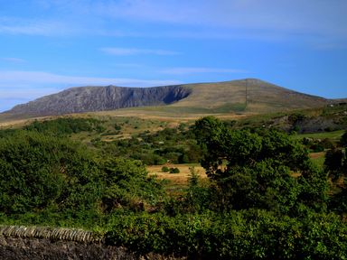 A landscape with trees, bushes, grassy fields and a mountain under a blue sky at 60 Hyfrydle Road Talysarn near Caernarfon