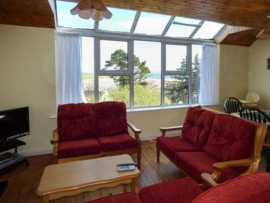 A living room with red cushioned sofas and a wooden coffee table in front of large windows overlooking trees at Number 12 Mulranny County Mayo