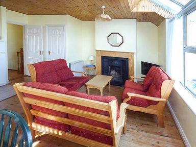 A living room with wooden ceiling red cushioned sofas coffee table fireplace and large window at Number 12 Mulranny County Mayo