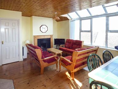 A living room with wooden sofas and a fireplace by large windows at Number 12 in Mulranny County Mayo
