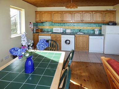 A kitchen with wooden cabinets and appliances beside a dining table with a vase of flowers at Number 12 in Mulranny County Mayo