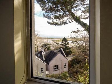 A view through a window showing a house with a black roof trees and a body of water in the background at Number 12 Mulranny County Mayo