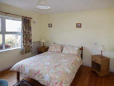 A bedroom with a double bed floral bedding two wooden bedside tables with lamps and a window with floral curtains at Number 12 in Mulranny County Mayo