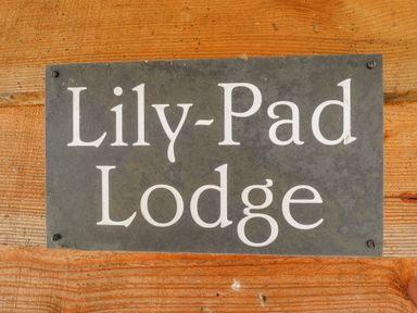 A metal sign with Lily-Pad Lodge mounted on a wooden wall at Lily-pad Lodge in Thorpe-on-the-Hill