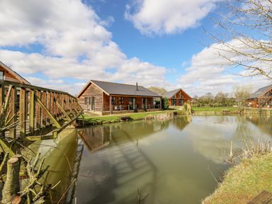 Cabins near a pond with a wooden bridge and trees at Lily-pad Lodge in Thorpe-on-the-Hill