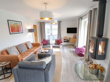 A living room with a leather sofa gray armchairs a wood burning stove and a wall mounted TV at Lily-pad Lodge in Thorpe-on-the-Hill