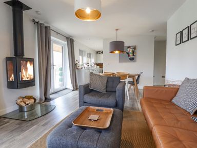 A living room with a wood burning stove armchairs a dining table and kitchen visible in the background at Lily-pad Lodge in Thorpe-on-the-Hill