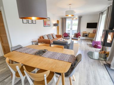 A dining area with a wooden table and chairs next to a living room with sofas and a wall-mounted tv at Lily-pad Lodge in Thorpe-on-the-Hill
