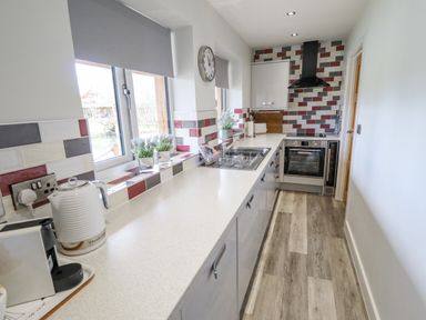 A narrow kitchen with countertop appliances sink stove and tiled backsplash at Lily-pad Lodge in Thorpe-on-the-Hill