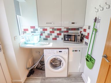 A laundry room with a washing machine vacuum cleaner microwave and laundry basket at Lily-pad Lodge in Thorpe-on-the-Hill