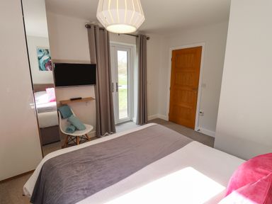 A bedroom with a bed a television on the wall a white chair with towels and a wooden door at Lily-pad Lodge in Thorpe-on-the-Hill