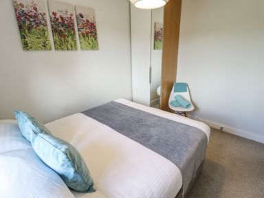A bedroom with a bed blue pillows and a gray runner a white chair with towels and a wardrobe with mirror at Lily-pad Lodge in Thorpe-on-the-Hill