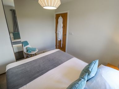 A bedroom with a bed pillows a chair with towels a mirror a wooden door and a hanging robe at Lily-pad Lodge in Thorpe-on-the-Hill
