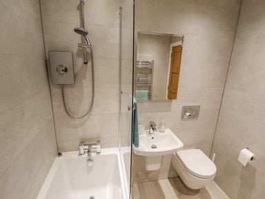 A bathroom with a bathtub shower combination a wall-mounted sink a toilet and a mirror at Lily-pad Lodge in Thorpe-on-the-Hill