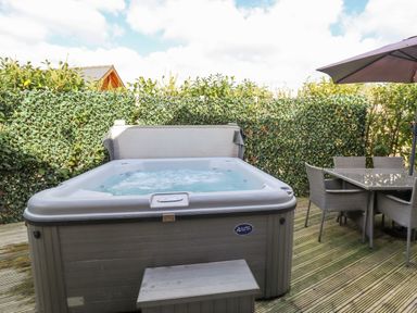 An outdoor deck area with a hot tub and a dining table with chairs and umbrella at Lily-pad Lodge in Thorpe-on-the-Hill