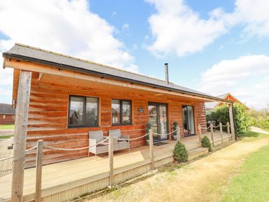 A wooden lodge with a covered porch and outdoor chairs at Lily-pad Lodge in Thorpe-on-the-Hill