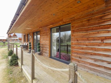 A wooden cabin exterior with a deck and potted plants at Lily-pad Lodge in Thorpe-on-the-Hill