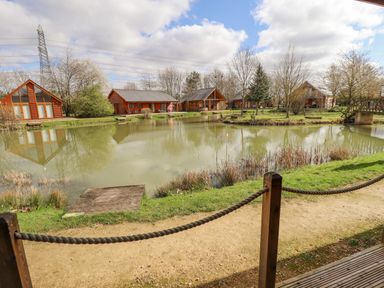 A pond with wooden lodges around it and a pathway with a rope fence at Lily-pad Lodge in Thorpe-on-the-Hill