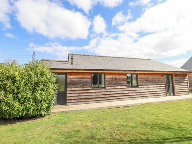 An exterior view of a wooden cabin with a gray roof and green bushes on a grassy lawn at Lily-pad Lodge in Thorpe-on-the-Hill