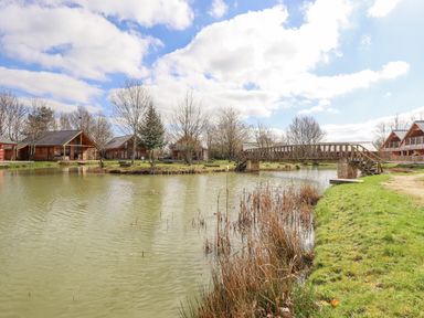 A pond with a wooden bridge and cabins around at Lily-pad Lodge in Thorpe-on-the-Hill