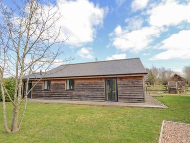 A wooden cabin with a sloped roof and glass doors on a grassy area at Lily-pad Lodge in Thorpe-on-the-Hill