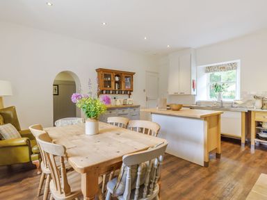 A kitchen with a wooden dining table and chairs a kitchen island cabinets and a window at Gardeners Cottage in Bellingham