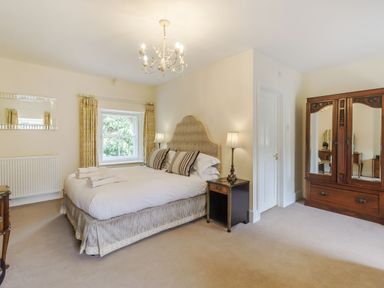 A bedroom with a double bed bedside tables lamps a window with curtains and a wooden mirrored wardrobe at Gardeners Cottage in Bellingham
