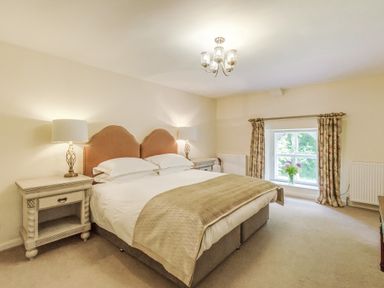A bedroom with a double bed bedside tables with lamps a window with curtains and a vase of flowers at Gardeners Cottage in Bellingham