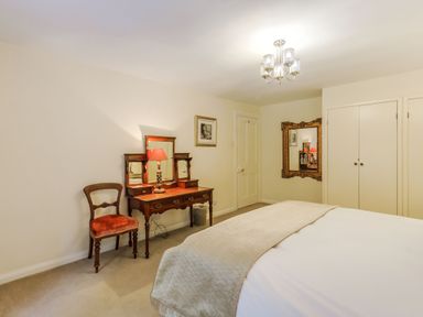 A bedroom with a wooden dressing table a chair a bed with beige bedding and a large mirror at Gardeners Cottage in Bellingham