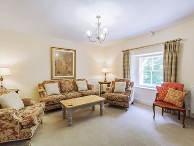 A sitting room with patterned sofas a wooden coffee table and a window with curtains at Gardeners Cottage in Bellingham