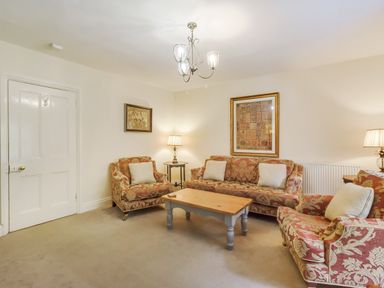 A living room with patterned sofas a wooden coffee table wall art and lamps at Gardeners Cottage in Bellingham
