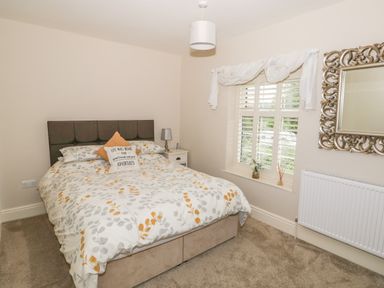 A bedroom with a bed a bedside table with a lamp a window with blinds and a decorative mirror at Bertelle in Grimston