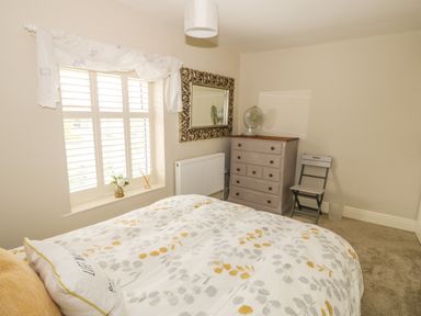 A bedroom with a bed a dresser a mirror a window with shutters and a chair at Bertelle in Grimston