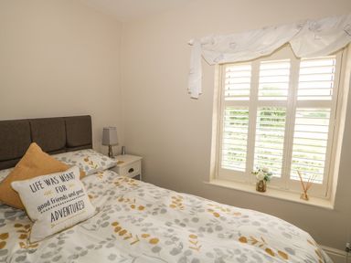 A bedroom with a bed a bedside table lamp and a window with shutters and flowers on the sill at Bertelle in Grimston