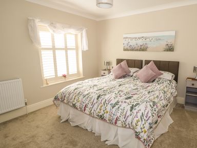 A bedroom with a double bed floral bedding bedside tables lamps and a window with shutters at Bertelle in Grimston