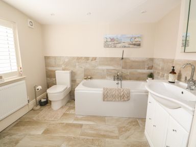 A bathroom with a toilet bathtub and sink with beige tile flooring and walls at Bertelle in Grimston
