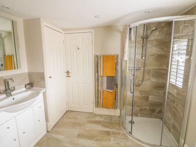A bathroom with a curved glass shower, a towel rack with towels, a sink with a cabinet, and two white doors at Bertelle in Grimston