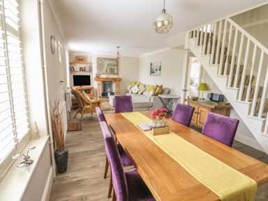 A dining area with a wooden table and purple chairs next to a living room with a beige sofa and a fireplace at Bertelle in Grimston
