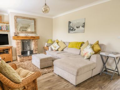 A living room with a beige sofa and cushions a wicker chair a brick fireplace and a television at Bertelle in Grimston