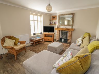 A living room with a gray sofa a wicker chair a fireplace a television and wooden furniture at Bertelle in Grimston