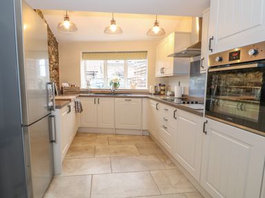 A kitchen with white cabinets a stainless steel refrigerator built in oven and a window with a roller blind at Bertelle in Grimston