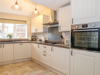 A kitchen with white cabinets a built in oven and stove under hanging lights at Bertelle in Grimston
