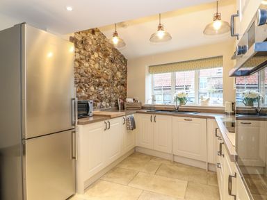 A kitchen with stainless steel refrigerator stone feature wall and white cabinets at Bertelle in Grimston