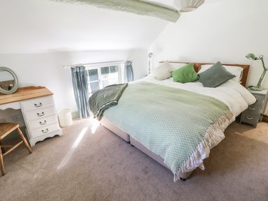 A bedroom with a bed covered in green and white bedding beside a white nightstand with a green lamp and a desk with a round mirror at Town Mill in Bewdley