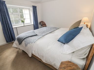A bedroom with a bed pillows a wooden bedside table a lamp blue curtains and a window at Town Mill in Bewdley