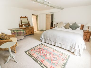 A bedroom with a double bed with pillows bedside tables a dresser with a mirror an armchair and a patterned rug on the floor at Town Mill in Bewdley