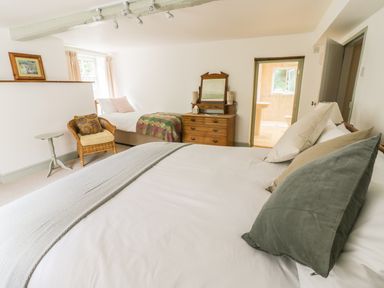 A bedroom with two beds a wicker chair a wooden dresser and an open door to a bathroom at Town Mill Bewdley