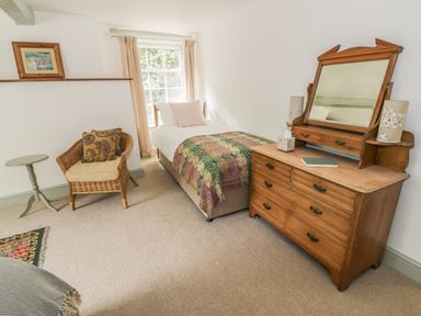 A bedroom with a single bed a wooden dresser with mirror a wicker chair and a small round table at Town Mill in Bewdley