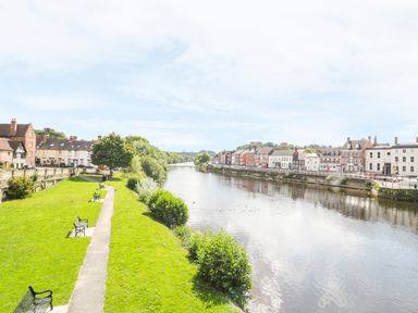 A river with buildings on both sides and benches along a pathway near the water at Town Mill in Bewdley